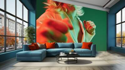 Futuristic man in stylish outfit with sunglasses, dancing against a vibrant green and red background, embodying modernity and exploration of technology in everyday life Wall mural