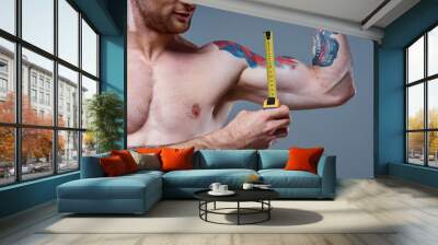 guy measures arm muscles with centimeters on a gray background and a multicolored tattoo bodybuilder fitness Wall mural