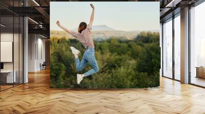 Happy woman jumping up from happiness in nature with her back to the camera with a beautiful mountain view Wall mural