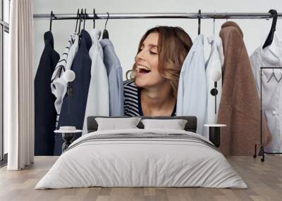 Happy woman peeking out from behind clothes in dressing room shopping youth Wall mural