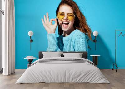 marks with fingers woman joyful in glasses on blue background Wall mural