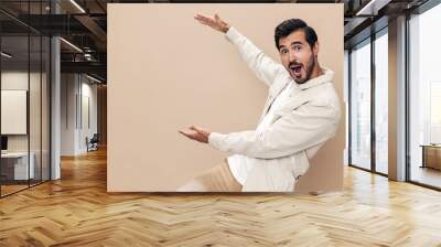 Portrait of a stylish man smile with teeth and surprise raised his hands up on a beige background in a white t-shirt, fashionable clothing style, copy space, space for text Wall mural