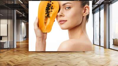 Portrait of a woman holding a papaya in front of her face and looking at the camera in natural lighting Wall mural