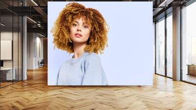 Portrait of a young woman with curly hair against a light blue background, exuding confidence and natural beauty with a soft expression Wall mural