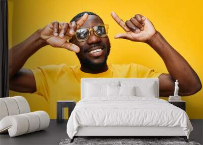 Smiling man in yellow t shirt with glasses against bright yellow background, showing positive emotions and playful gesture, expressing joy and enthusiasm Wall mural