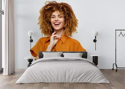 Smiling woman with curly hair, wearing an orange shirt, standing against a light background Her cheerful expression conveys positivity and confidence, ideal for lifestyle themes Wall mural