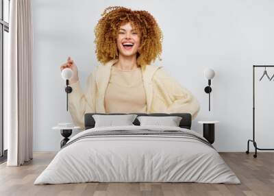 Smiling woman with curly hair wearing a cozy sweater against a plain light background, conveying joy and confidence Perfect for lifestyle and fashion content Wall mural