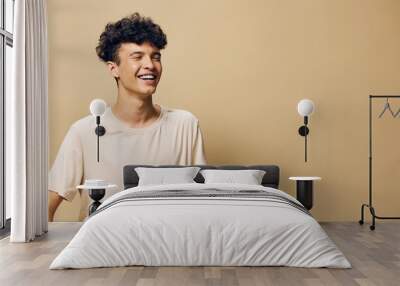 Smiling young man in a light beige t shirt against a soft brown background, expressing happiness and joy, showcasing a carefree and positive lifestyle Wall mural