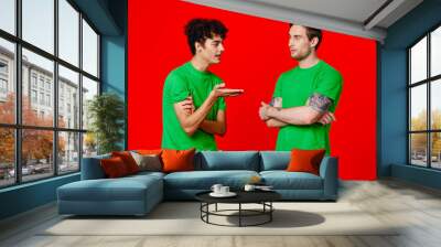 two friends in green t-shirts are standing side by side communication positive red background Wall mural