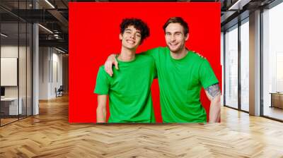 two friends in green t-shirts hugs fun red background Wall mural