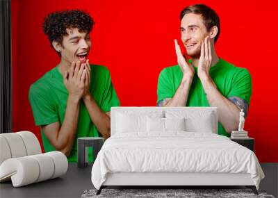 two men holding their heads in green T-shirts on a red background Wall mural