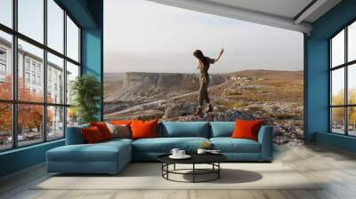 Woman embracing nature and freedom on top of a rock in the middle of a field Wall mural