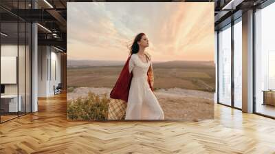 Woman in white dress standing on top of a hill with sunset in background, travel beauty nature fashion concept Wall mural