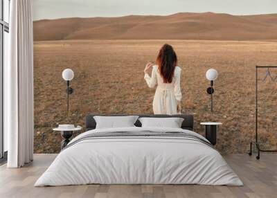 Woman in white dress walking through open field in desert during fashion photoshoot under the sun's embrace Wall mural