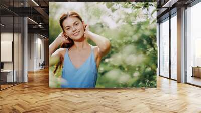 Woman smile with teeth in profile happiness in nature in the summer near a green tree in the garden of the park in a blue dress, the concept of women's health and beauty with nature sunset Wall mural