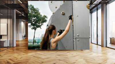 Young woman climbing a modern rock wall in an outdoor park setting Wall mural