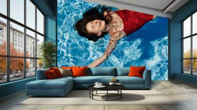 Young woman in the pool in a red swimsuit with a beautiful smile lying on the water and swimming in the sun swimming in the pool, the concept of relaxing on vacation. Wall mural