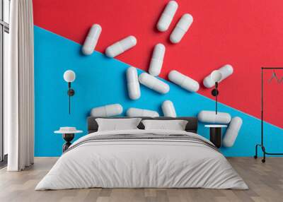 White medicine capsules on blue and red background Wall mural