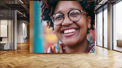 Young black woman with curly hair and glasses laughing in front of a vibrant wall in a portrait Wall mural