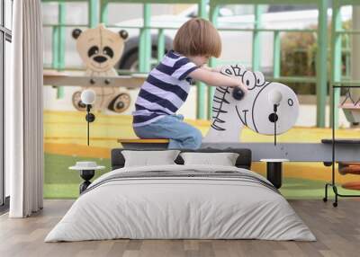 Happy baby child riding a toy white horse at the playground. Boy 3 years with long hair Wall mural