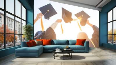 Graduation day celebration students wearing caps and gowns raise their hats high in joyful triumph against a bright sky Wall mural