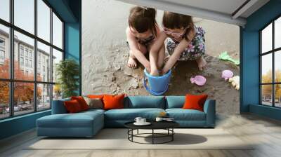 Two little girl plays in the sand on the beach on a summer holiday. Wall mural