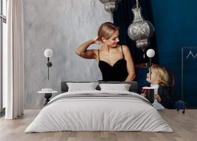 Elegant mother in black dress with little son on the sofa. Blue background Wall mural