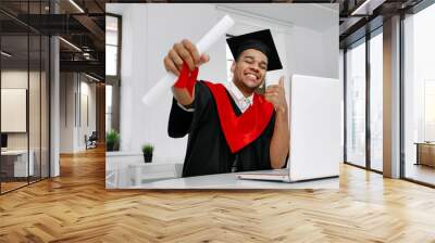 A Black student in graduate gown and square cap who is happy to finish his studies shows his the long-awaited diploma Wall mural