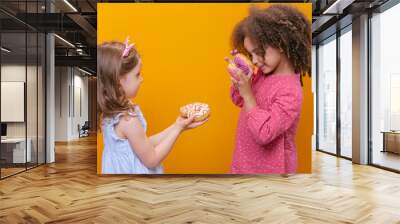 The girls are holding donuts in their hands on a yellow background. An African-American girl is playing with sweets. Wall mural