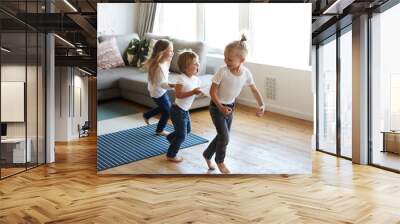 Action freeze shot of three happy joyful children one girl and two boys pullin each other by clothes while doing conga line, screaming in joy and excitement. Happiness, childhood and leisure Wall mural