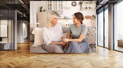 Beautiful happy mature mother and her adorable cute daughter spending time together after long separation, sitting in cozy living room interior and talking, looking at each other and smiling Wall mural