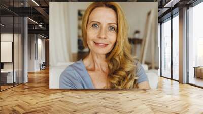 Caucasian adult woman of 50s wearing no makeup up, having natural beauty, perfect ageing face skin, covered with freckles, some face lines and wrinkles, sitting against home interior background Wall mural