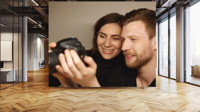 Happy l young Caucasian man and his wife holding digital camera and viewing pictures taken during honeymoon, choosing good photos to get them printed. People, relationships and modern technology Wall mural