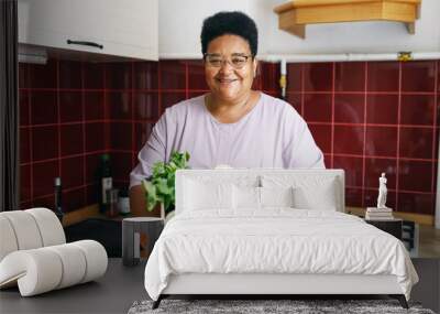 Happy smiling contented overweight african american woman of 60s holding big card box with fresh vegetables standing at kitchen against counter, after receiving her food delivery service order Wall mural