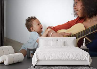 Happy young Hispanic female musician sitting on floor, playing guitar to her adorable cute baby son who is singing along with her, Music, art, talent, creativity, infancy, education and childcare Wall mural