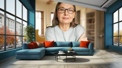 Horizontal portrait of senior gray haired European female in eyeglasses posing indoors, looking at camera with serious facial expression. Mature people, aging, retirement and lifestyle concept Wall mural