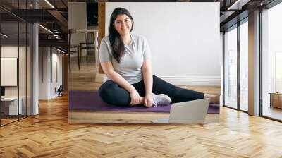 Indoor image of beautiful energetic young plus size woman with curvy body training at home to lose weight and get strong flexible body, wearing sneakers, exercising on mat, watching video on laptop Wall mural