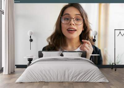 Indoor shot of energetic attractive young female manager in eyeglasses talking to colleagues online during video conference call while working from home, social distancing, using modern technology Wall mural