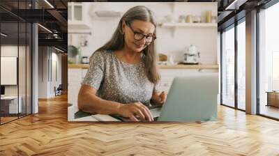 Inspired older woman typing on laptop. Elderly smiling lady composing story on device, work from home. Hobby for soul, creativity, inspiration, technology concept Wall mural