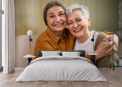 Joy, fun and happiness. Indoor shot of happy senior female in shirt hugging her short haired female friend laughing at joke, enjoying nice time together. Two middle aged best friends relaxing Wall mural