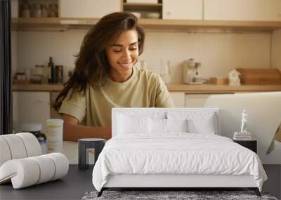 Nutrition, healthy lifestyle and body hacking. Joyful young woman nutritionist sitting in front of open laptop, having online consultation, entering information about dietary supplement in her hand Wall mural