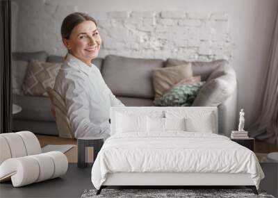 People, aging, technology, occupation and lifestyle concept. Indoor shot of cheerful beautiful senior businesswoman in white shirt working from home office, sitting at desk and smiling happily Wall mural