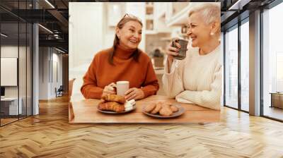 People, lifestyle and leisure concept. Portrait of stylish senior women in cozy sweaters having breakfast together at cafe, sitting at wooden table, sharing news, drinking coffee with pastries Wall mural