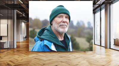 People, maturity age, retirement, nature, recreation and adventure concept. Portrait of handsome smiling senior male pensioner with thick gray beard, wrinkles and blue eyes walking outdoors Wall mural