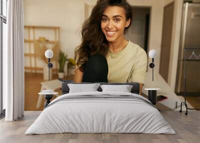 Pretty adorable young female freelancer sitting on table with open laptop, having break while working distantly from home, having relaxed joyful facial expression. Leisure and domesticity Wall mural