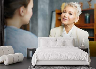 Psychology, consulting and coaching concept. Stylish middle aged female psychologist having conversation with brunette woman client, discussing problems and progress, sitting in her cozy office Wall mural