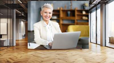 successful fifty year old businesswoman with short blonde hair and radiant smile communicating onlin Wall mural