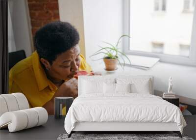 Upper side view image of plus size african american senior retired woman eating juicy fresh organic grapefruit sitting at table near window, being on diet, loosing weight to be healthy Wall mural