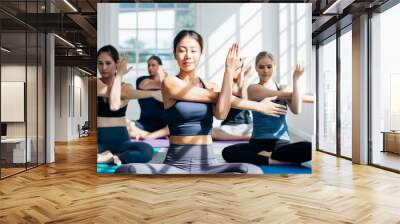 Group of young sporty attractive people practicing yoga lesson with instructor. Instructor woman leading exercise pose, Healthy lifestyle, working out, indoor full length, studio background. Wall mural