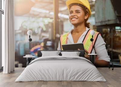 Industry maintenance engineer woman dark skin wearing uniform and safety helmet under inspection and checking production process on factory station by tablet. Industry, Engineer, construction concept. Wall mural